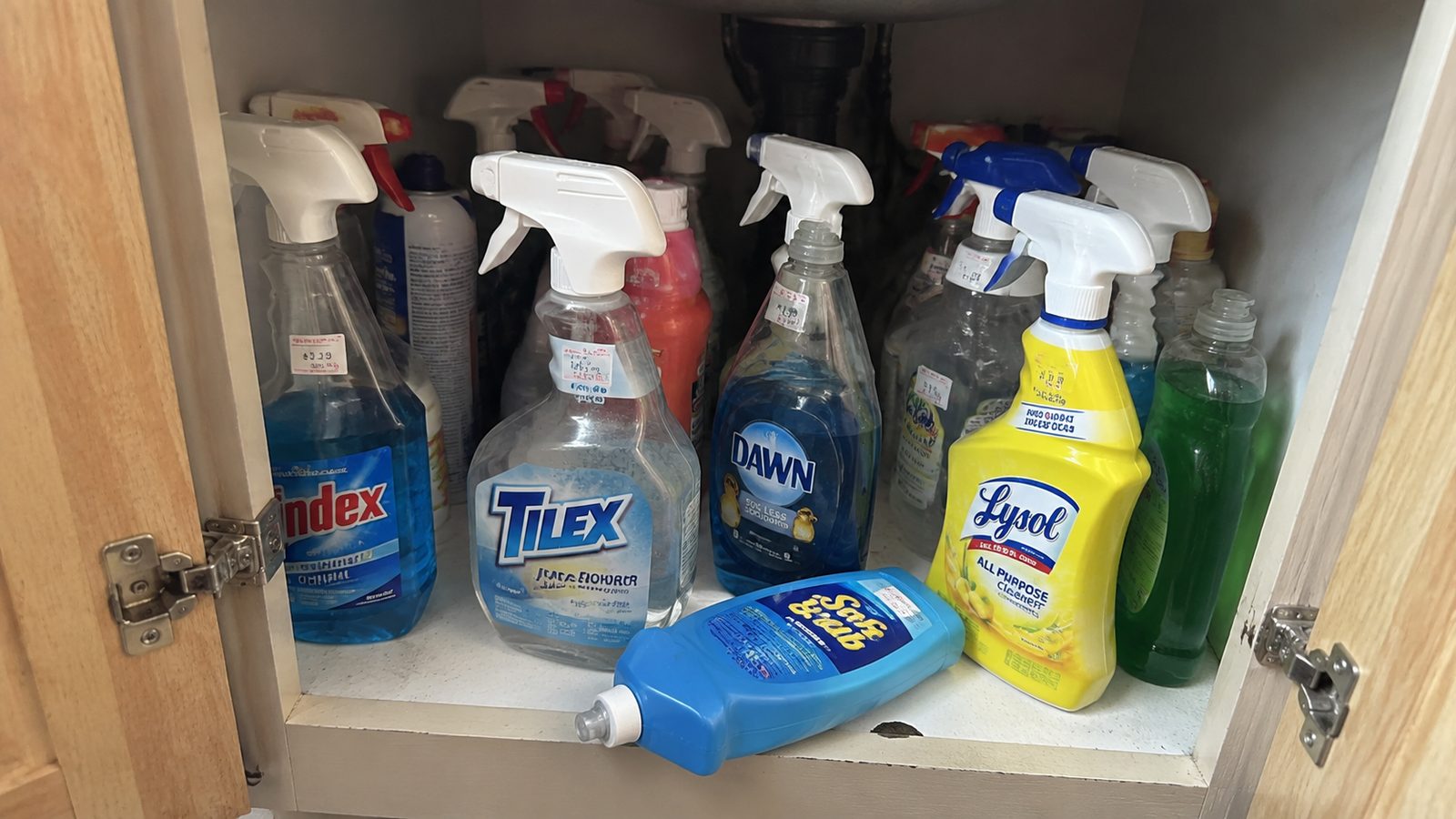 A cupboard under a kitchen sink crowded with a dozen half-used branded cleaning sprays